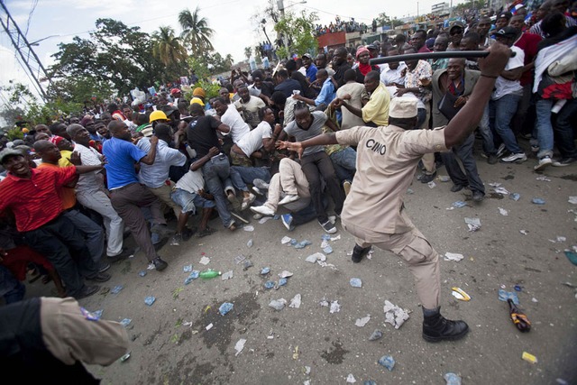 Một cảnh sát dùng dùi đánh người biểu tình ủng hộ cựu Tổng thống Haiti, Jean-Bertrand Aristide ở Port-au-Prince.
