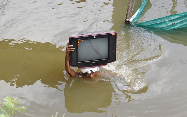 Một người đàn ông đội tivi trên trong khi lội trong nước lũ ở Allahabad, Ấn Độ.