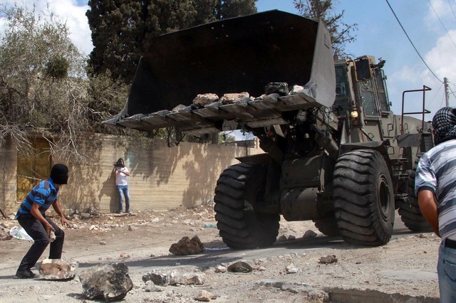 Một người Palestin bịt mặt chuẩn bị ném đá vào xe ủi đất của quân đội Israel trong cuộc biểu tình chống xây dựng các khu định cư của người Do Thái tại thành phố Nablus, Bờ Tây.