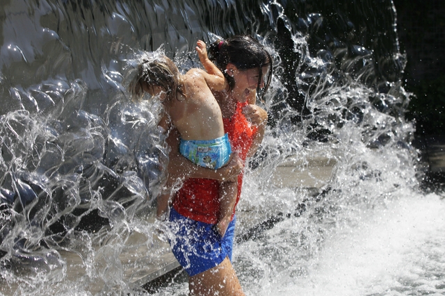 Hai mẹ con hạ nhiệt bằng cách đi qua một thác nước trong công viên Yards ở Washington, Mỹ, khi nhiệt độ ở khu vực này lên tới hơn 35 độ C.