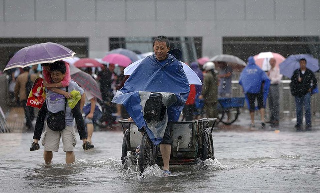 Mọi người di chuyển khó khăn trên đường phố ngập lụt do mưa bão ở thành phố Thượng Hải, Trung Quốc.