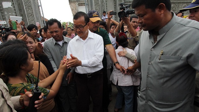 
	Lãnh đạo Đảng Cứu quốc đối lập Sam Rainsy (áo trắng) chào cử tri trước cổng một địa điểm bỏ phiếu ở tỉnh Kandal, nơi ông vừa đi bầu