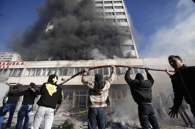 Người biểu tình giúp đỡ lính cứu hỏa dập tắt một đám cháy bùng phát tại tòa nhà chính phủ ở Tuzla, Bosnia & Herzegovina.
