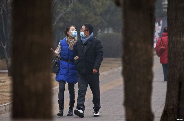 Cặp đội đeo khẩu trang đi dọc một đường phố trong sương mù ở Bắc Kinh, Trung Quốc.