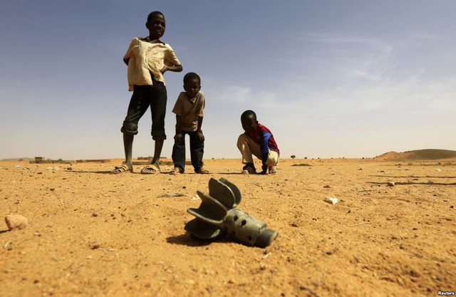 Trẻ em nhìn phần đuôi của một quả đạn cối được phát hiện tại trại tị nạn Al-Abassi sau một vụ tấn công của phiến quân ở thị trấn Mellit, Sudan.
