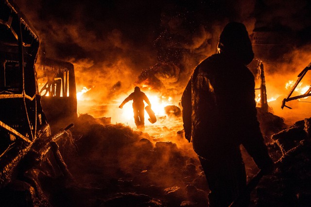 Những người biểu tình chống chính phủ đi qua những chiếc lốt xe bị đột cháy trên đường phố ở Kiev, Ukraine.