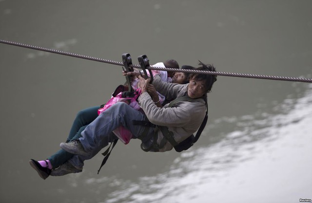 Một người đàn ông cùng vợ và con nhỏ đu dây thép qua sông Nujiang ở Nộ Giang, Vân Nam, Trung Quốc.