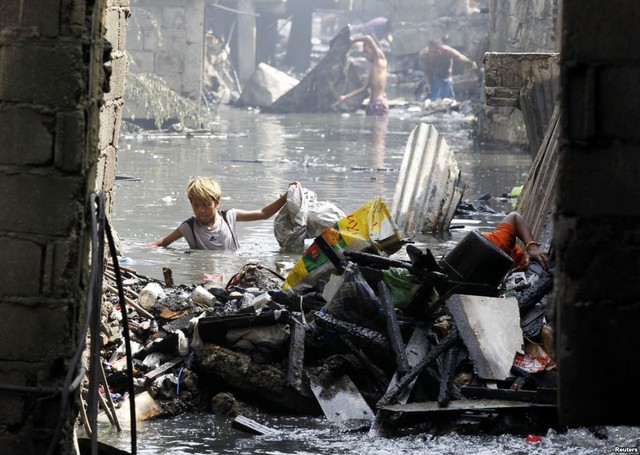 Một cậu bé lội qua con lạch để nhặt những đồ có thể tái chế sau vụ hỏa hoạn tại khu ổ chuột ở Caloocan, Philippines.