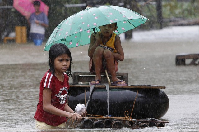 Bé gái kéo bè tự chế chở em trai dọc một đường phố ngập lụt ở Butuan, Philippines.