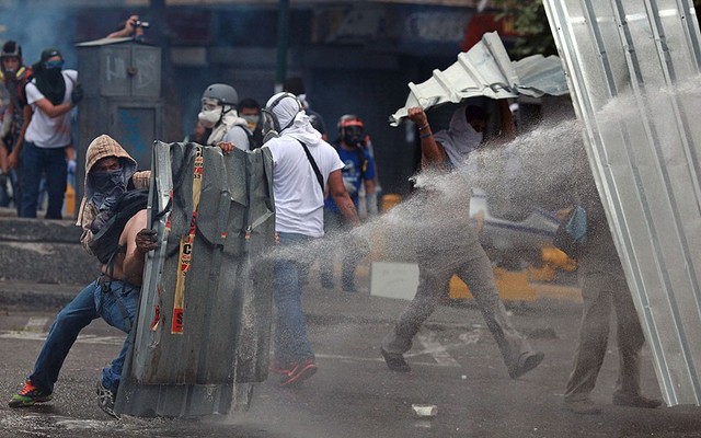 Những người biểu tình dùng tấm tôn để che khi cảnh sát phun voi rồng trên đường phố ở Caracas, Venezuela.
