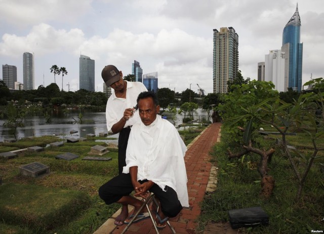 Quản trang Mohammad Udin được cắt tóc bởi một thợ cắt tóc rong tại một nghĩa trang ở Jakarta, Indonesia.