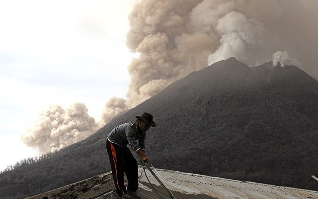 Một người dân dọn tro bọi trên mái nhà trong khi núi lửa Sinabung tiếp tục phun trào mạnh ở Karo, Indonesia.