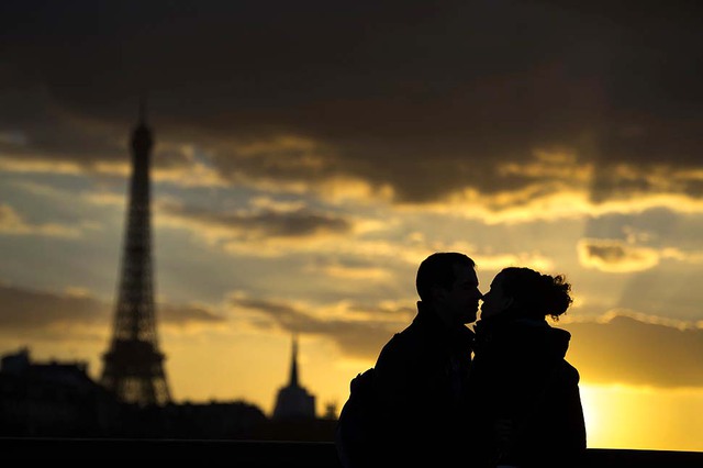 Một cặp đôi hôn nhau lãng mạn trước tháp Eiffel khi mặt trời lặn ở Paris, Pháp.