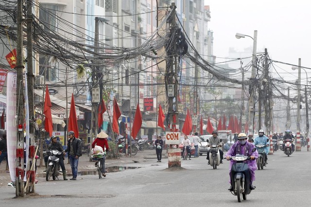 Các phương tiện đi qua cột điện với dây chằng chịt trên một đường phố ở Hà Nội, Việt Nam.