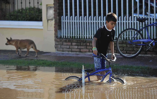 Một cậu bé dắt xe đạp qua đường phố ngập lụt do mưa lớn ở Lujan, Buenos Aires, Argentina.
