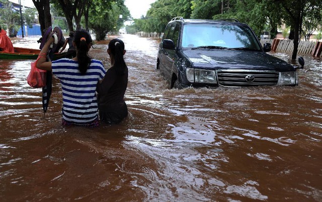 Người dân lội trên đường phố ngập lụt khi một chiếc ô tô đi qua ở Jakarta, Indonesia.