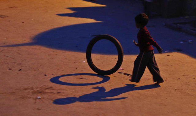 Một cậu bé chơi với lốp xe bên ngoài nhà gần đường ray tàu hỏa ở New Delhi, Ấn Độ.