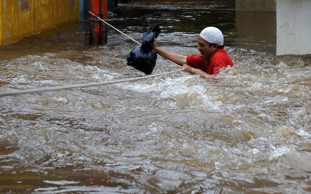 Một người đàn ông cầm dây để lội qua dòng nước lũ ở Kampung Melayu, Jakarta, Indonesia.