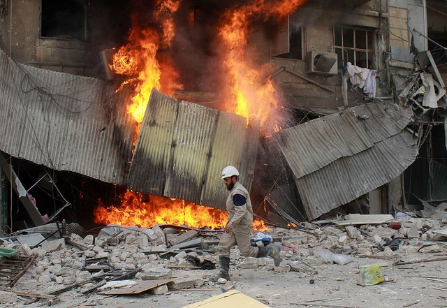 Một thành viên của đội cứu hộ chạy trước tòa nhà bị cháy sau vụ thả bom của quân đội chính phủ ở Aleppo, Syria.