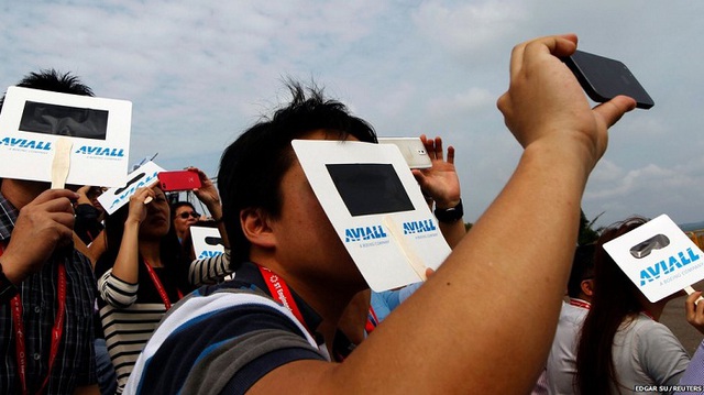 Khán giả sử dụng các tấm bìa để bảo vệ mắt khỏi ánh nắng mặt trời khi xem triển lãm hàng không Singapore Airshow.