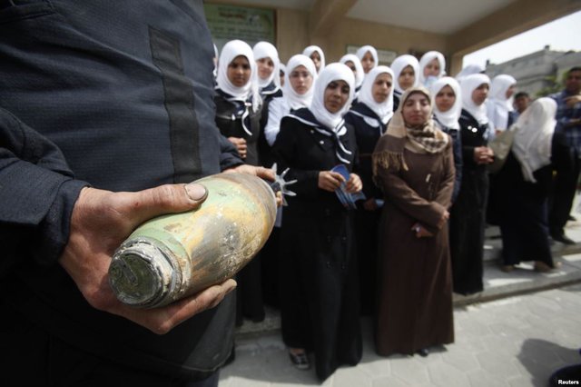 Một thành viên của lực lượng an ninh Palestine cầm một quả đạn cối, khi giải thích cho những người phụ nữ về sự nguy hiểm của quả đạn tại trường học ở Khan Younis, Dải Gaza.