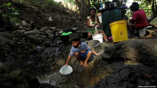 Một cậu bé lấy nước trong khi những người phụ nữ ngồi giặt quần áo ở ngoại ô thành phố Panama City, Panama.