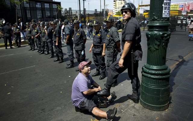 Thợ đánh giày đánh boot cho một cảnh sát chống bạo động đứng thành hàng rào để ngăn chặn người biểu tình diễu hành ở Lima, Peru.