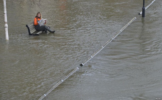 Một phụ nữ ngồi trên ghế bên bờ sông Thames ngập lụt ở Staines, Anh.