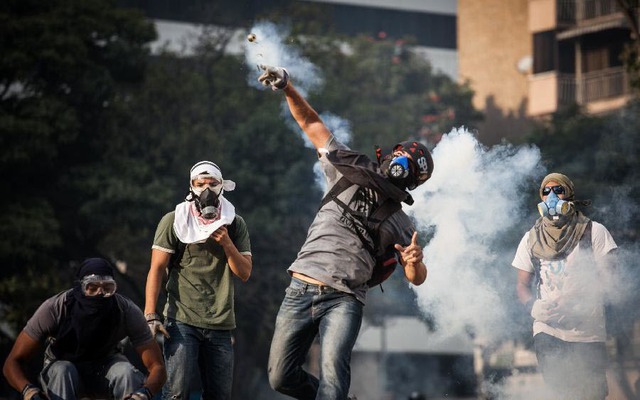 Người biểu tình ném lựu đạn hơi cay trở lại cánh sát chống bạo động trong cuộc đụng độ ở Altamira, Venezuela.