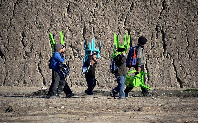 Học sinh đội ghế nhựa trên đầu trong khi đi tới trường ở Mazar-i-Sharif, Afghanistan.