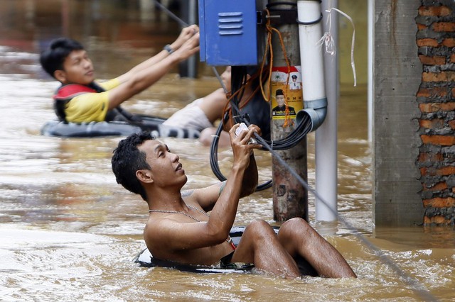 Mọi người đu dây để di chuyển trên đường phố ngập lụt ở Jakarta, Indonesia. Lũ lụt đã khiến 130.000 người dân Indonesia phải sơ tán.