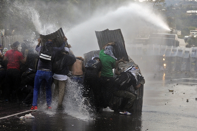 Người biểu tình che chắn khỏi vòi rồng của cảnh sát trên đường phố ở Caracas, Venezuela.