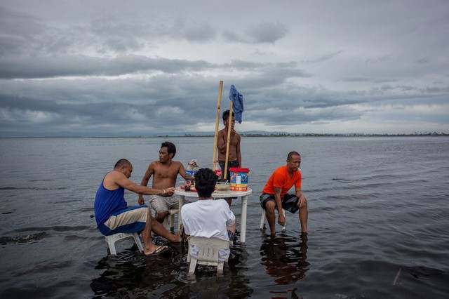 Những người đàn ông nghỉ ngơi và uống rượu dừa quanh bàn ngập nước trên bãi biển ở Tacloban, Philippines.