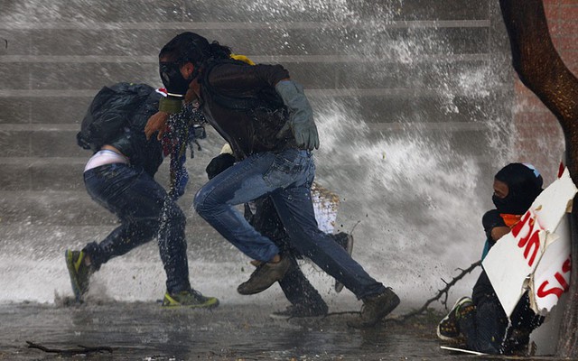 Người biểu tình chống chính phủ chạy khỏi vòi rồng phun nước của cảnh sát ở Caracas, Venezuela.