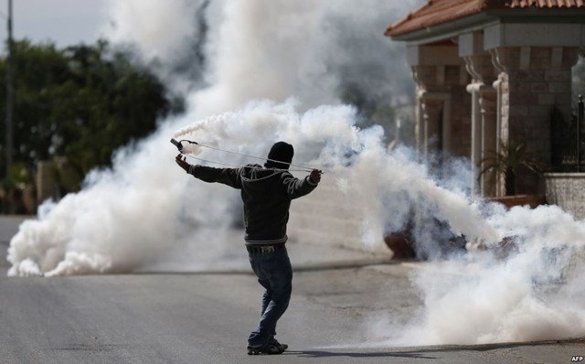 Một người Palestine sử dụng súng cao su để bắn lựu đạn hơi cay trở lại phía các binh sĩ Israel trong cuộc đụng độ ở Ramallah, Bờ Tây.