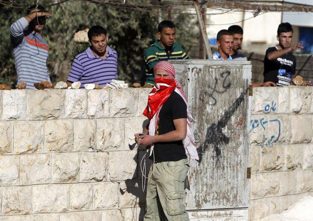Một thanh niên Palestine cầm súng cao su và đá đứng trước đồng đội trong cuộc đụng độ với lực lượng an ninh Israel, sau cuộc biểu tình phản đối kế hoạch mở rộng khu định cư Ofra của người Do Thái ở Bờ Tây.