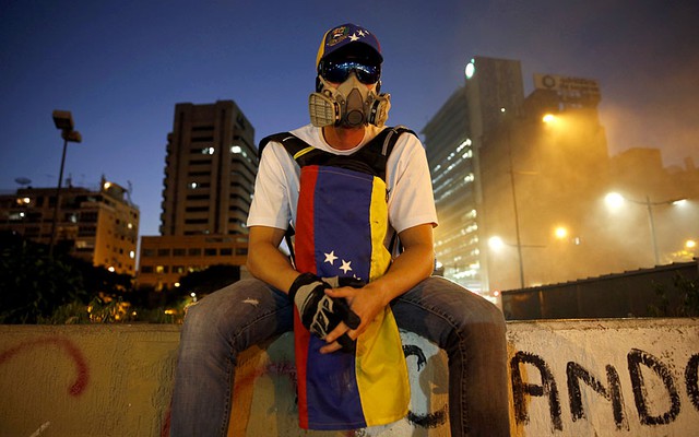 Một người biểu tình đeo mặt nạ phòng độc ngồi trên tường tại quảng trường Altamira ở Caracas, Venezuela.