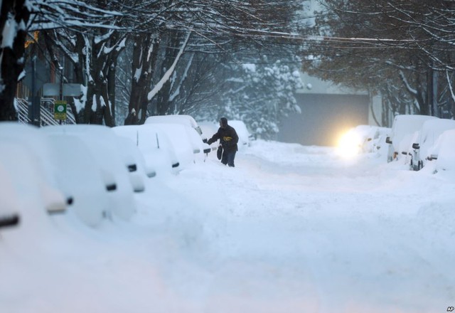 Một người đàn ông cố gắng mở cửa xe ô tô bị phủ đầy tuyết trên đường phố ở Albany, New York, Mỹ.