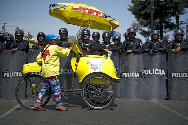Một phụ nữ bán kem trước cảnh sát chống bạo động giám sát cuộc biểu tình của thợ mỏ ở Lima, Peru.