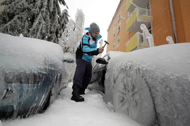 Một người đàn ông sử dụng búa để phá băng trên xe ô tô gần nhà ga ở Postojna, Slovenia.