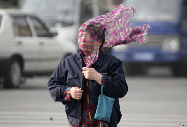 Gió mạnh thổi khăn che kín mặt một phụ nữ đi trên đường phố ở Thẩm Dương, Trung Quốc.
