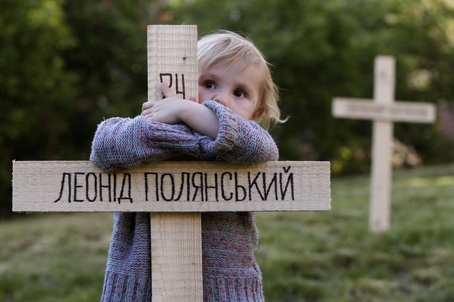 Bé gái ôm một trong số 107 chữ thập gỗ được dựng ở Prague để tượng niệm nạn nhân thiệt mạng trong các cuộc biểu tình gần đây ở Ukraine.
