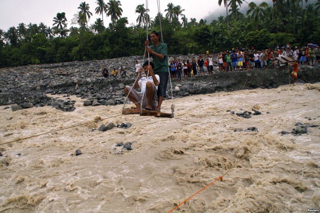 Người dân sử dụng cáp treo tự chế để chở người và hàng hóa qua sông với nước lũ chảy siết ở thị trấn New Bataan, tỉnh Compostela, Philippines.
