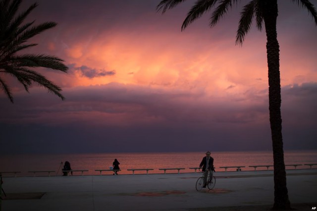 Một người đàn ông đạp xe dưới hoàng hôn trên bờ biển ở Barcelona, Tây Ban Nha.