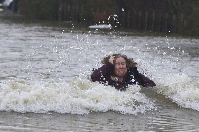 Một phụ nữ khó nhọc lội qua dòng nước lũ ở Old Windsor, Anh.