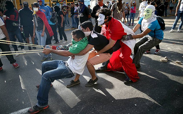 Người biểu tình hợp sức dùng súng cao su tự chế để bắn đá vào cảnh sát trong cuộc biểu tình chống chính phủ ở Caracas, Venezuela.
