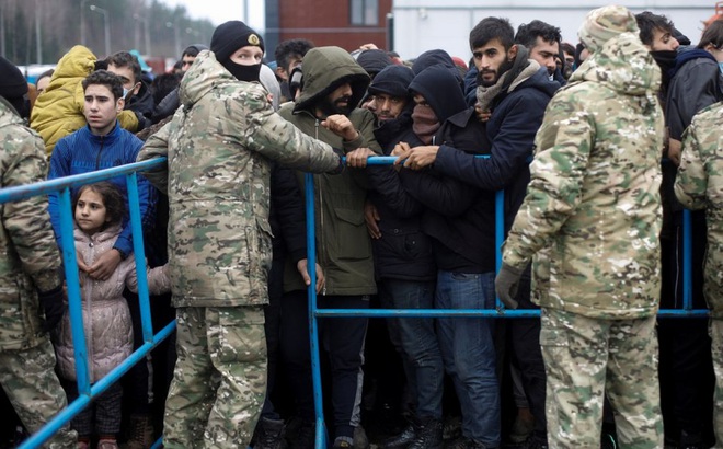 Lực lượng quân đội Belarus đứng cạnh hàng rào trong khi người di cư chen lấn để nhận lương thực bên ngoài trung tâm vận tải và hậu cần gần biên giới Belarus-Ba Lan ở vùng Grodno, Belarus ngày 21/11. Ảnh: Reuters