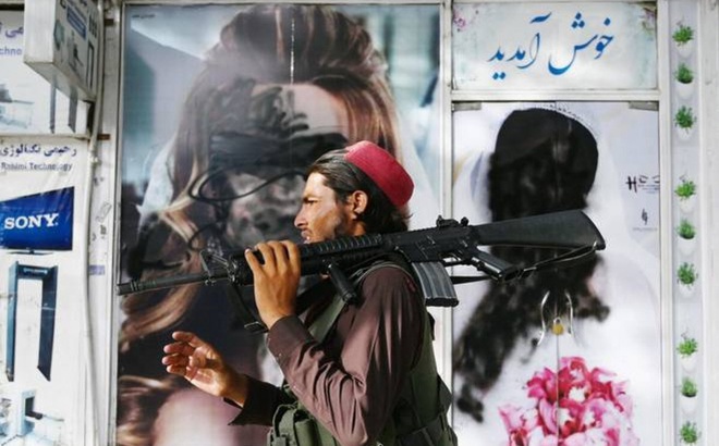 Một tay súng Taliban đi ngang qua cơ sở thẩm mỹ có hình phụ nữ trên tường đã bị phủ sơn ở Shar-e-Naw, Kabul, ngày 18/8/2021. Ảnh: AFP