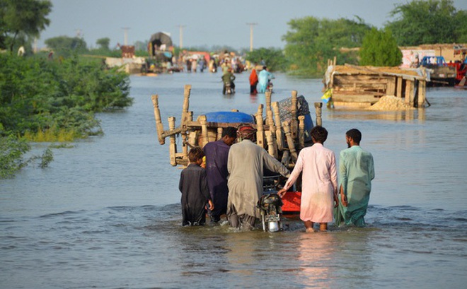 Những người đàn ông đi dọc con đường ngập lụt với đồ đạc của họ, sau mưa lũ trong đợt gió mùa ở Suhbatpur, Pakistan, ngày 28-8 - Ảnh: REUTERS