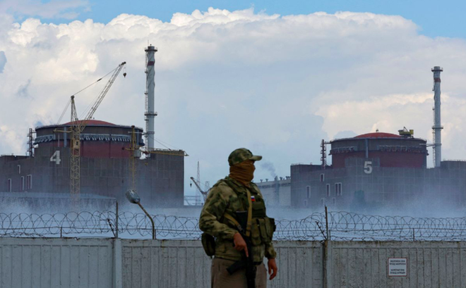 Một lính mặc đồng phục mang cờ Nga đứng canh trước nhà máy điện hạt nhân Zaporizhzhia. (Ảnh: Reuters)